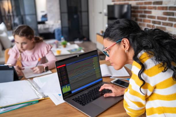 Young mother trading online on a laptop, while her daughter studies online via digital tablet. Young mother working on a laptop, while her daughter studies online via digital tablet. mom stock market stock pictures, royalty-free photos & images